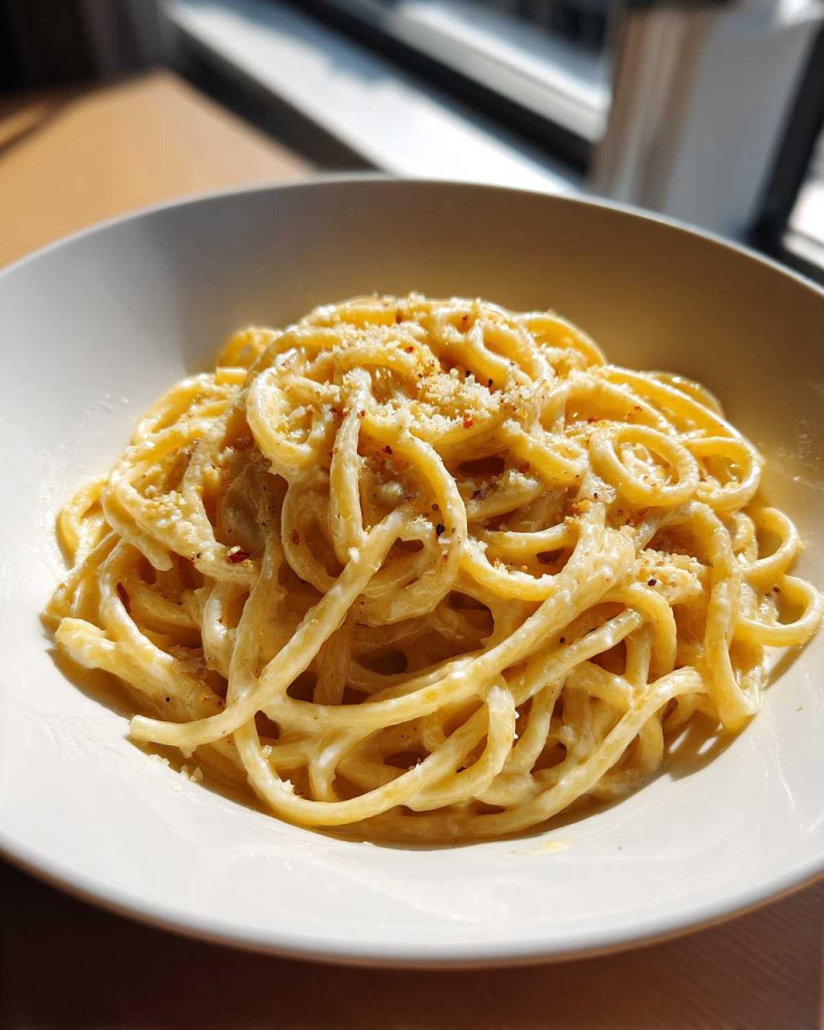 A close-up of spaghetti coated in creamy homemade alfredo sauce, topped with grated cheese and red pepper flakes.