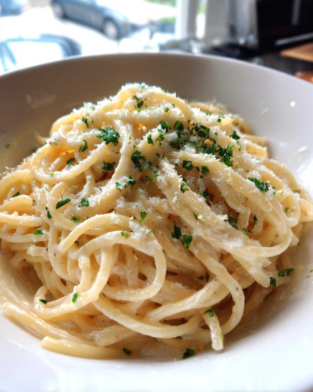 A close-up of spaghetti coated in creamy homemade alfredo sauce, topped with grated parmesan and parsley.