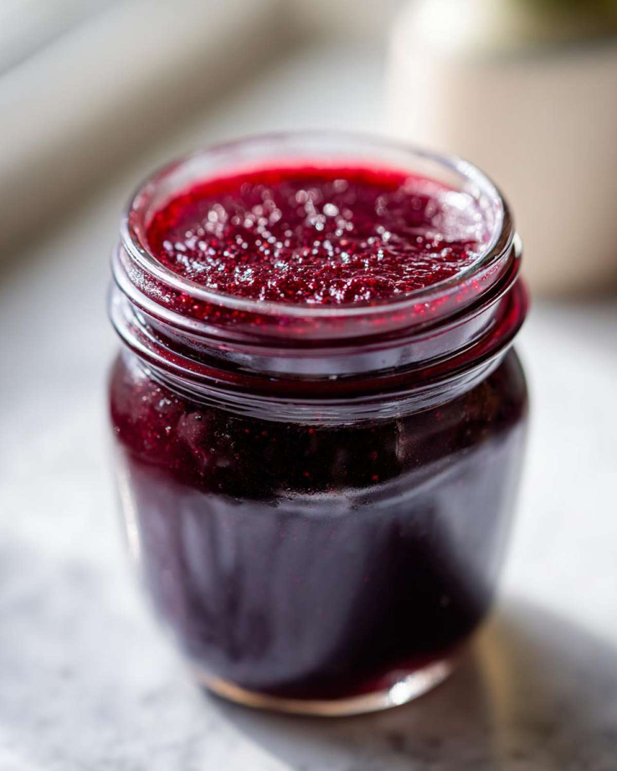 A close-up shot of a glass jar filled with glistening homemade grape jelly.
