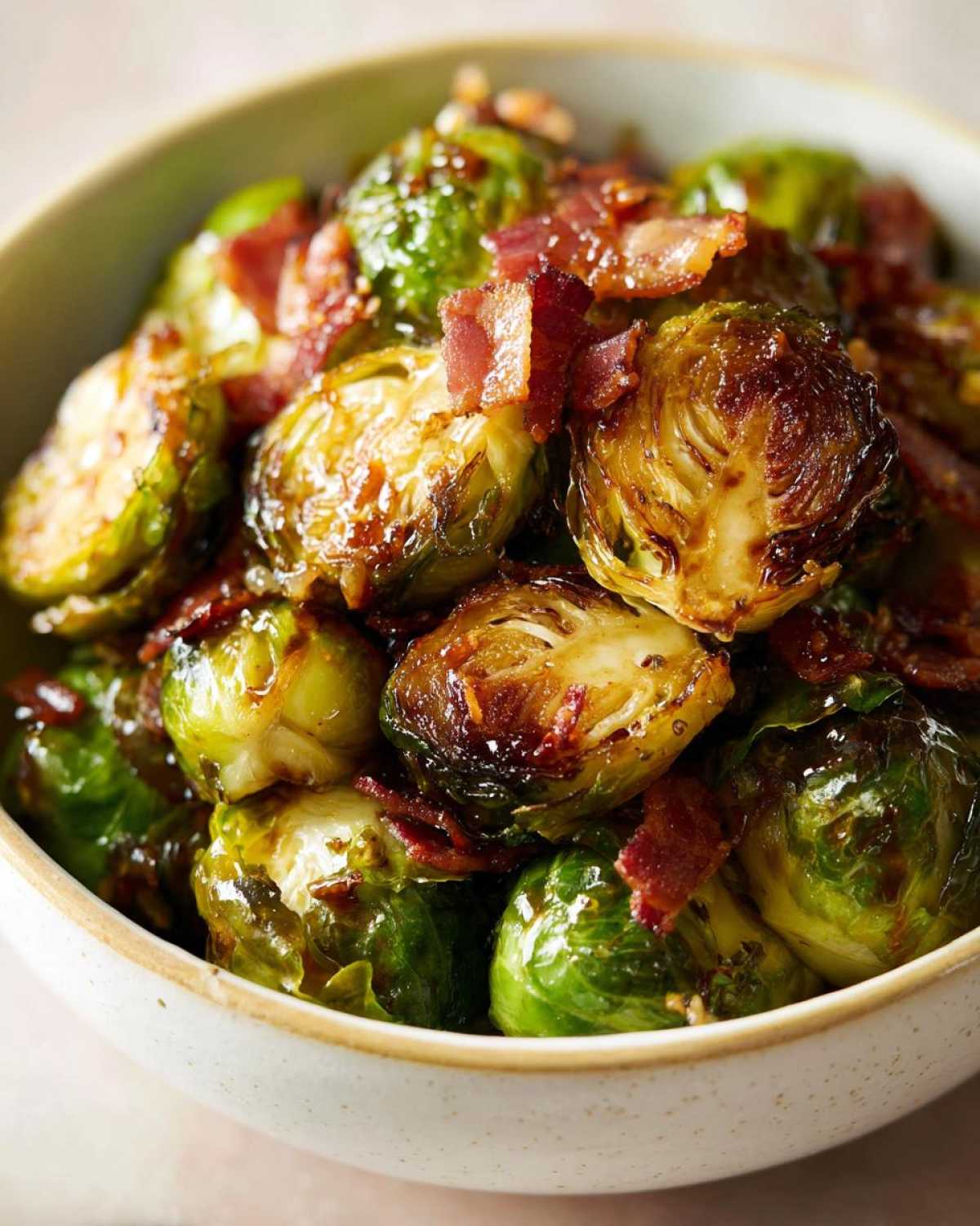 Close-up of crispy honey balsamic brussels sprouts topped with crumbled bacon in a bowl.