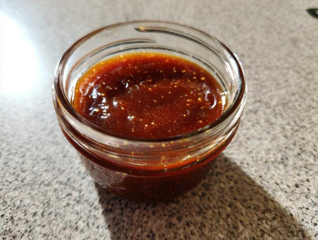 A small glass jar filled with glistening Honey BBQ sauce, showcasing its rich color and texture.