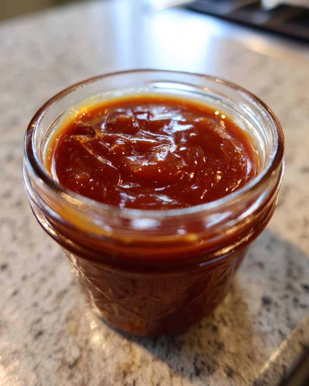 Close-up of a glass jar filled with thick, glossy Honey BBQ sauce.