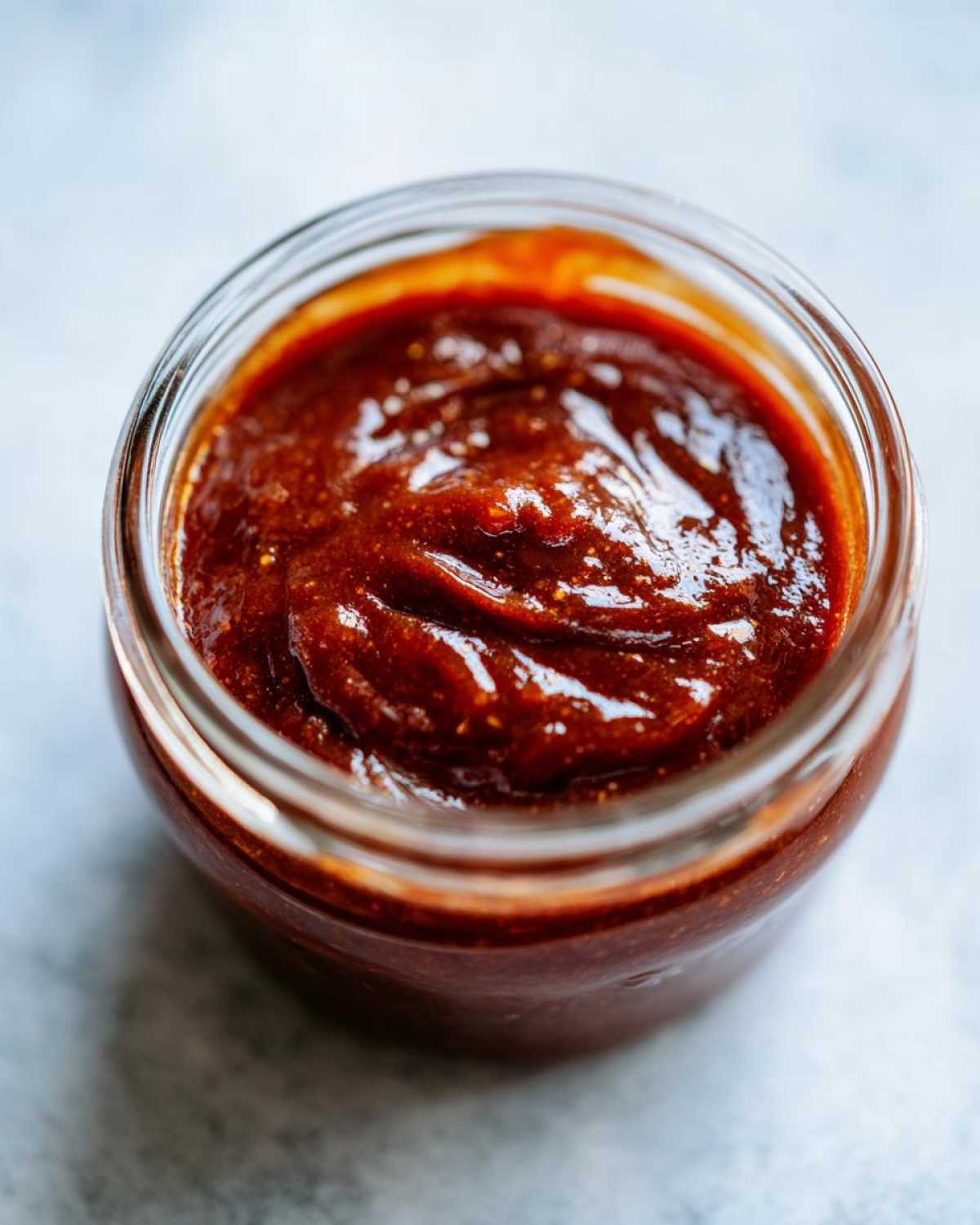 Close-up of a glass jar filled with rich, dark Honey BBQ sauce.