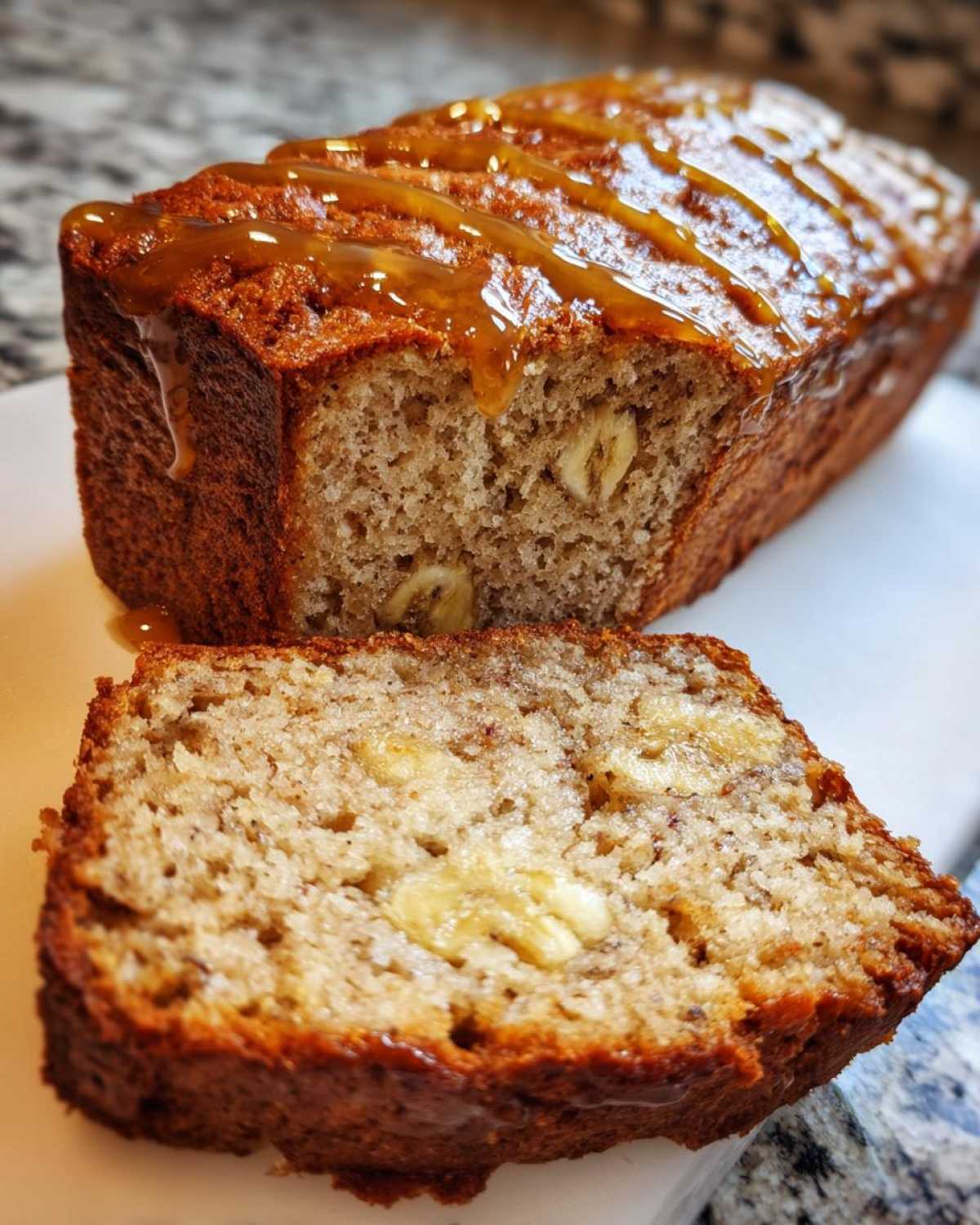 A slice of moist honey vanilla banana bread drizzled with caramel on a white cutting board.