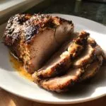 Close-up of juicy, sliced pork loin roast with a golden-brown crust on a white plate.