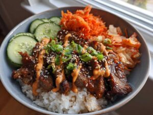 A close-up of a Korean BBQ steak rice bowl with tender steak, rice, kimchi, cucumber, and a drizzle of sauce.