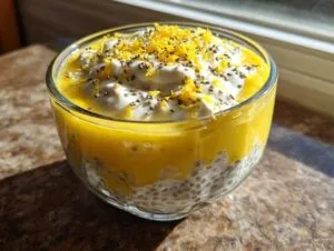 A close-up of a glass bowl filled with lemon cream chia pudding, topped with yogurt, chia seeds, and lemon zest.