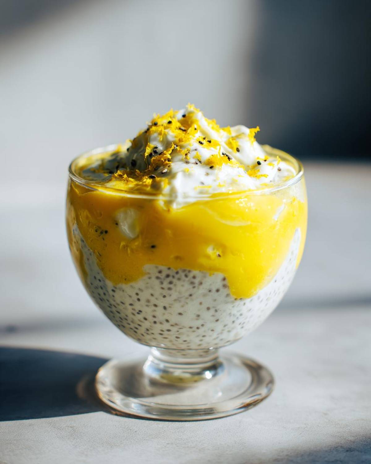 A vibrant glass of lemon cream chia pudding topped with mango puree and lemon zest.
