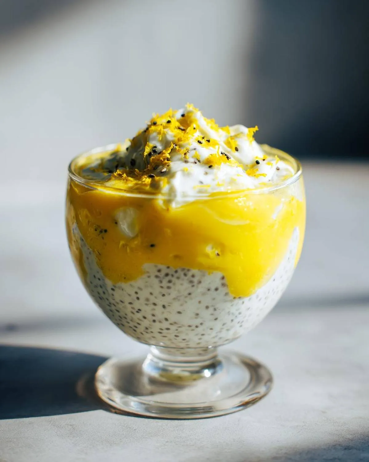A vibrant glass of lemon cream chia pudding topped with mango puree and lemon zest.