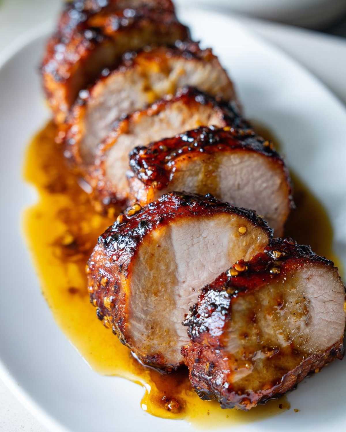 Close-up of sliced maple mustard pork tenderloin, glistening with sauce on a white plate.