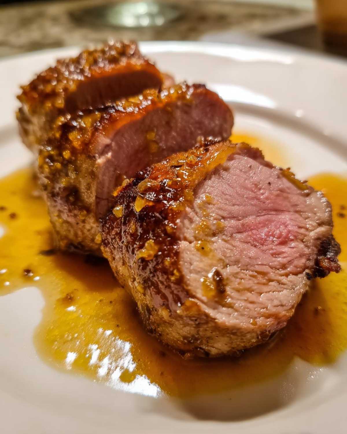 Close-up of a juicy maple mustard pork tenderloin, sliced and served with its glaze.