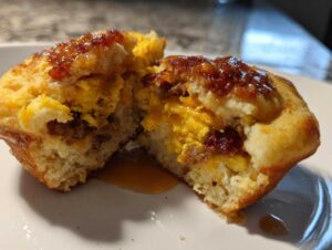 A close-up of a McGriddle muffin cut in half, revealing scrambled eggs, sausage, and a drizzle of syrup.