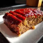 A close-up of a juicy meatloaf with a rich tomato glaze, sliced and served on a white plate.