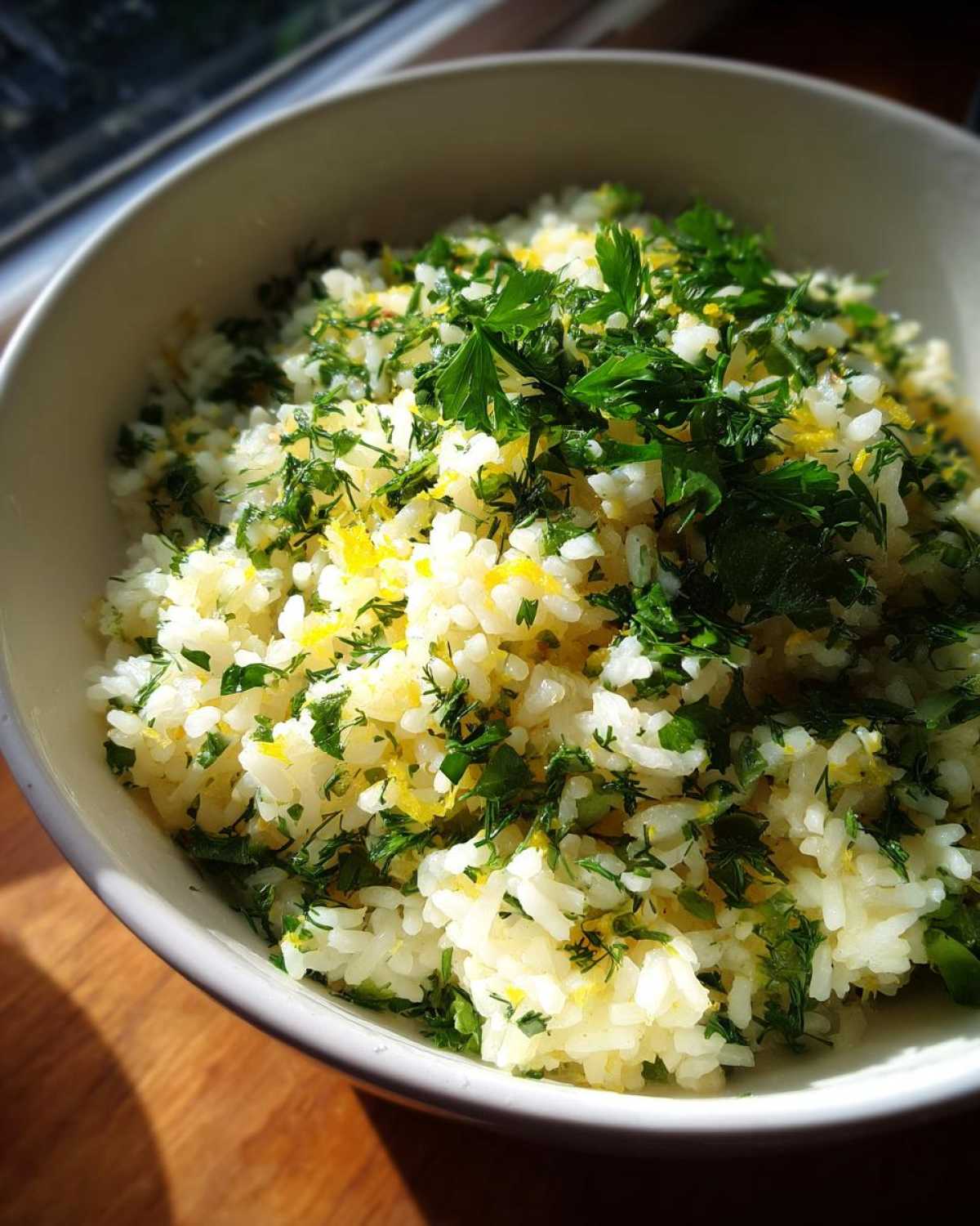 A bowl of fluffy Mediterranean lemon rice generously topped with fresh parsley and dill.