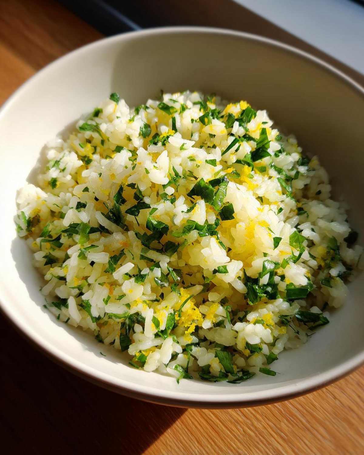 A close-up of a bowl of fluffy Mediterranean lemon rice, generously garnished with fresh parsley and lemon zest.