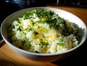 A close-up of a white bowl filled with fluffy Mediterranean lemon rice, topped with chopped fresh parsley and lemon zest.
