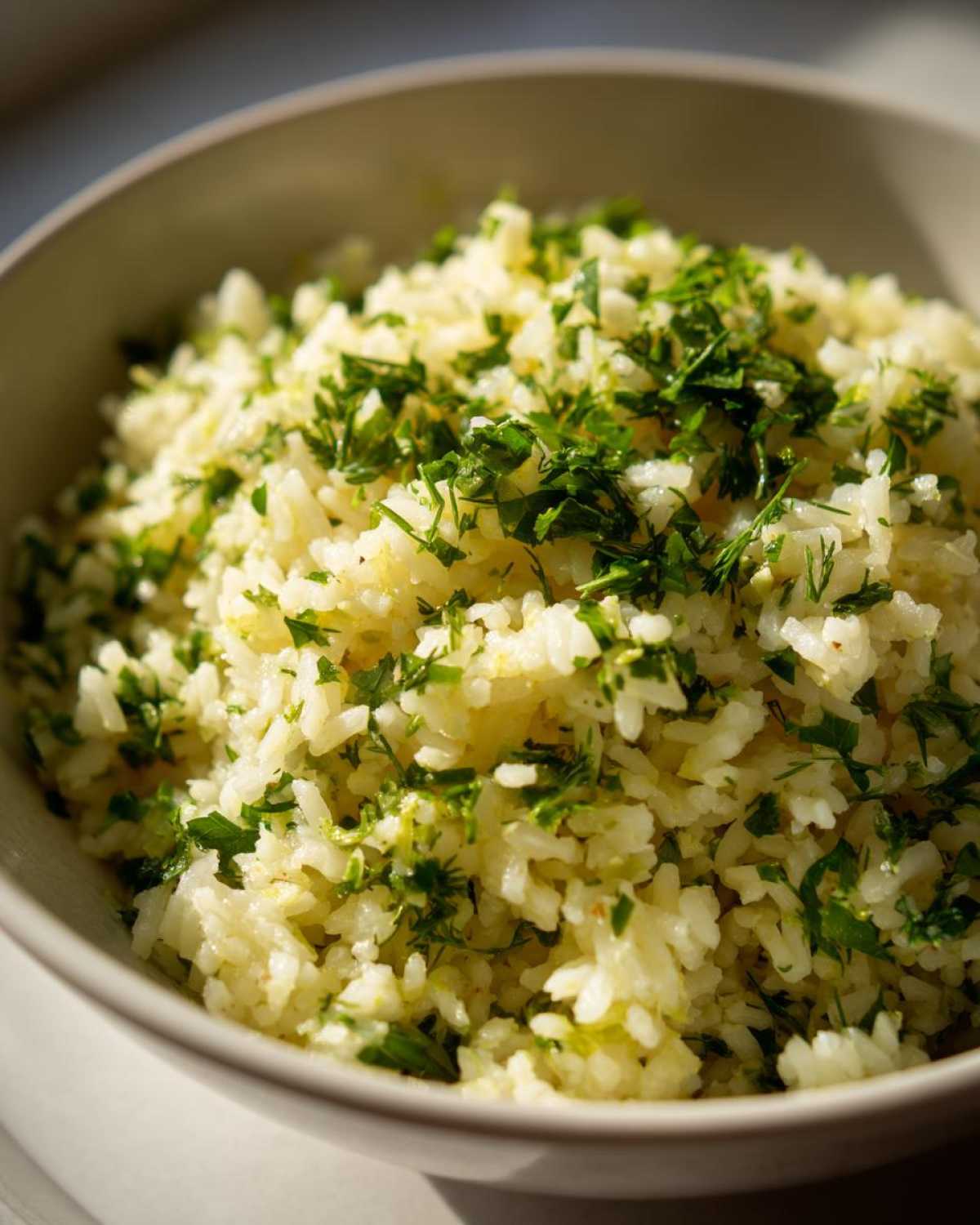 A close-up of fluffy Mediterranean lemon rice topped with chopped fresh parsley and dill.