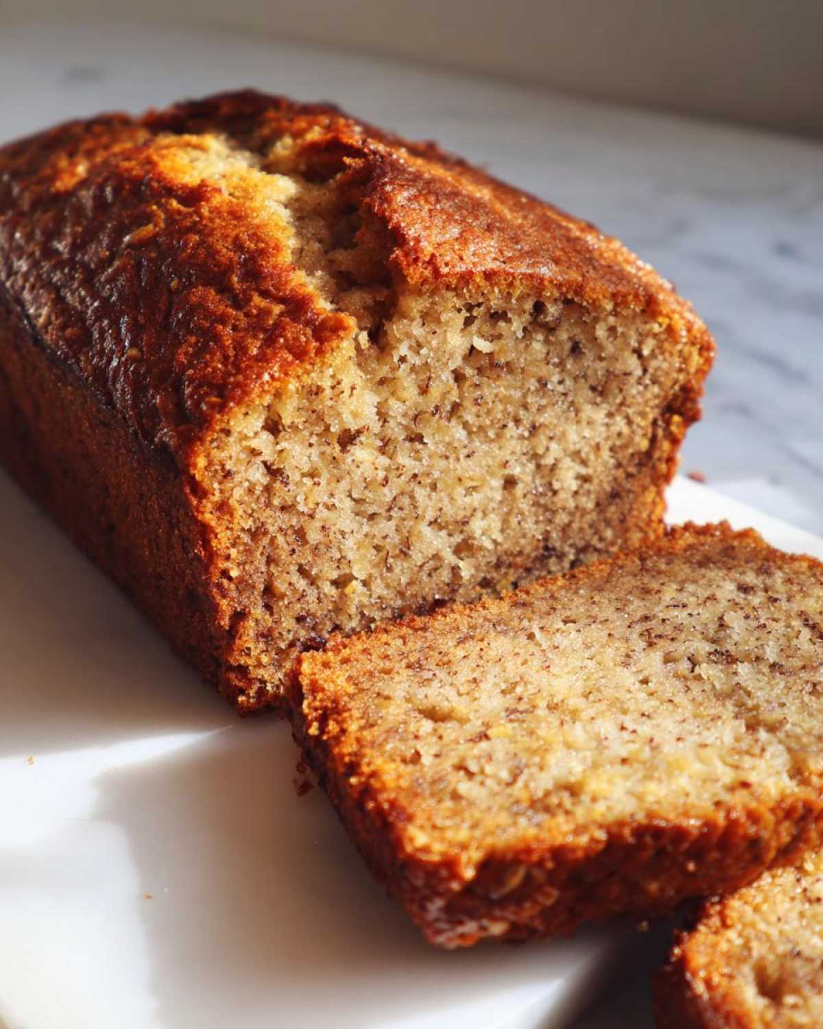 Close-up of a moist banana nut bread loaf with two slices cut, showing the texture.