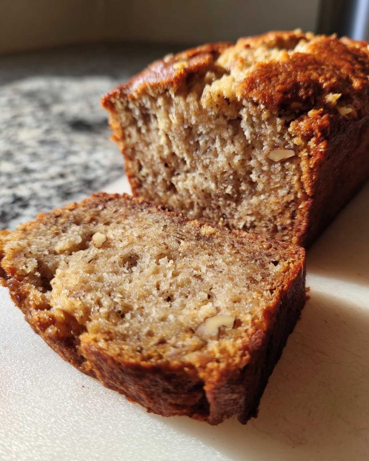 Close-up of a moist slice of banana nut bread with visible nuts and a golden-brown crust.