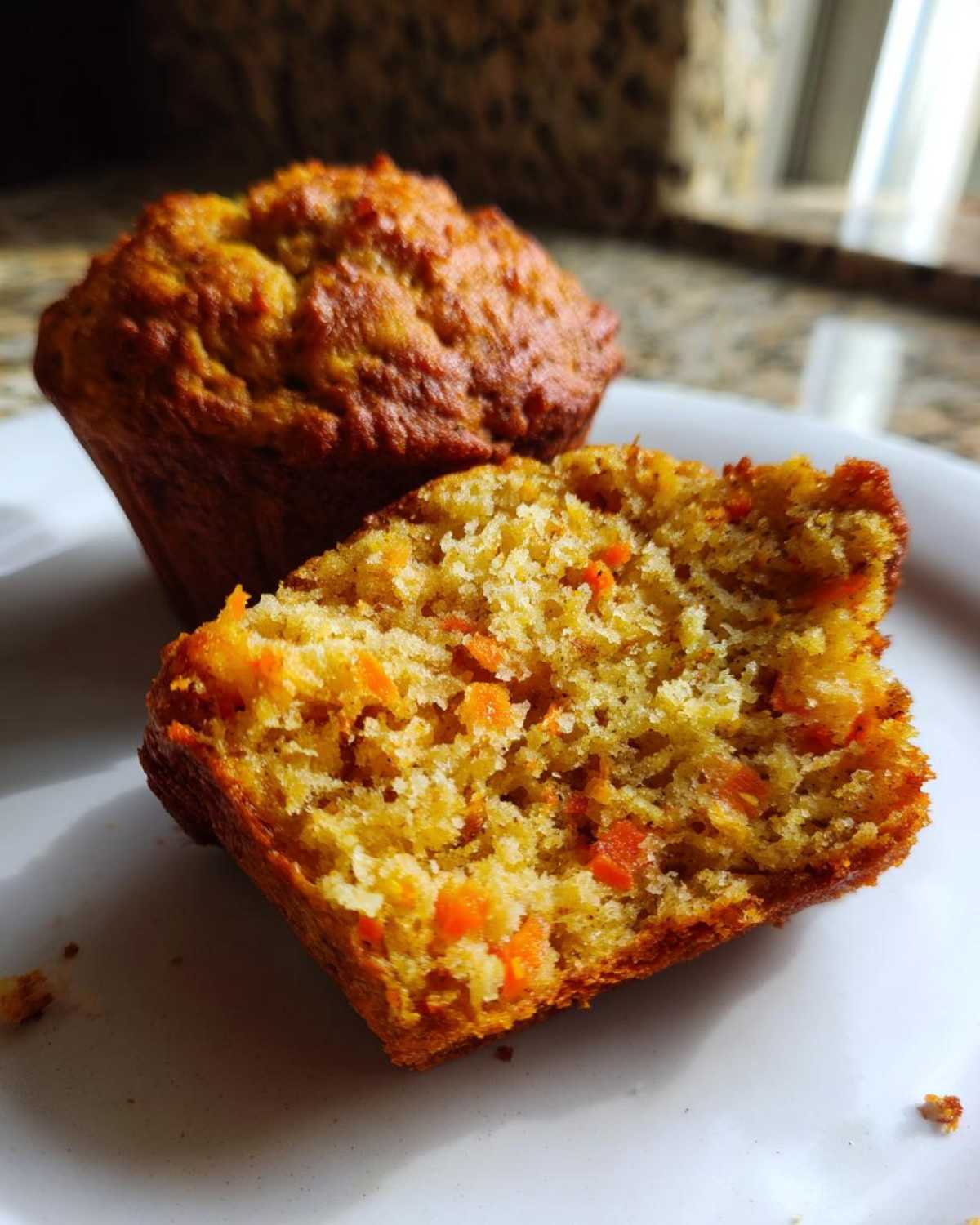 Close-up of a moist carrot muffin, cut in half, revealing visible chunks of carrot throughout the crumb.