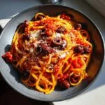A close-up of one pan spicy pasta topped with Kalamata olives and grated Parmesan cheese.