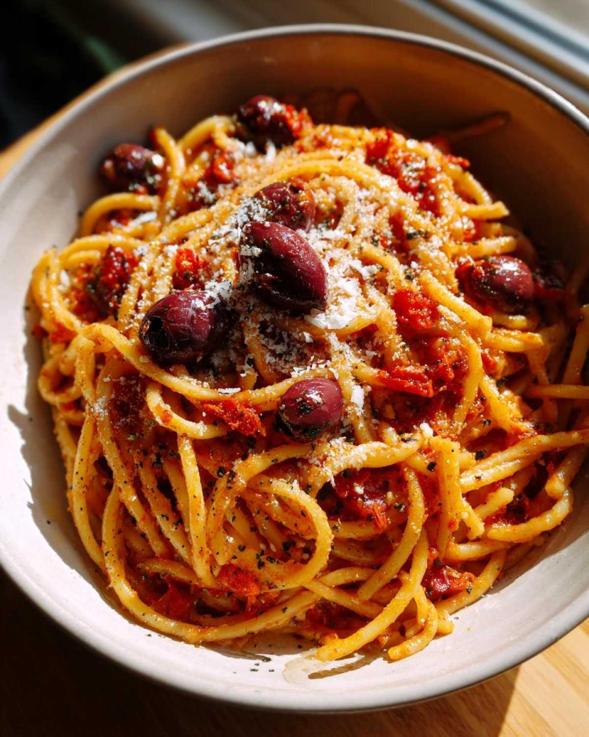 A bowl of one pan spicy pasta topped with Kalamata olives and grated Parmesan cheese.