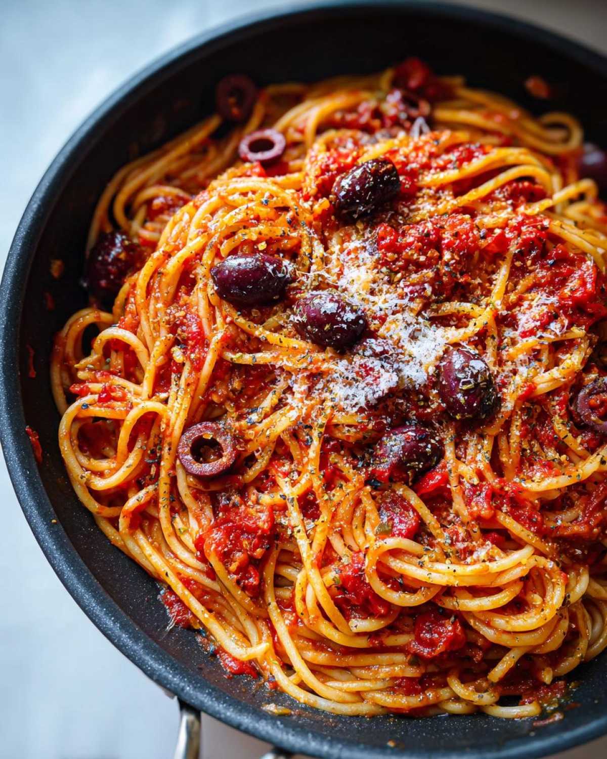 Close-up of a pan filled with one pan spicy pasta, topped with olives and grated parmesan cheese.