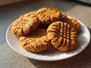 A close-up of several classic peanut butter cookies with criss-cross fork marks on a white plate.