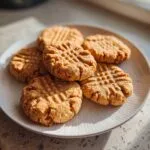 A close-up of several classic peanut butter cookies with fork marks on a white plate.