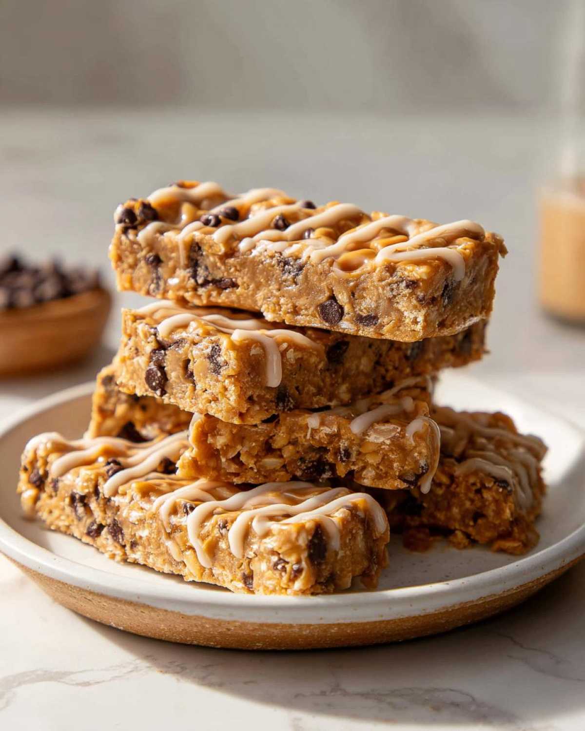 A stack of no-bake peanut butter protein bars drizzled with white icing and studded with chocolate chips.