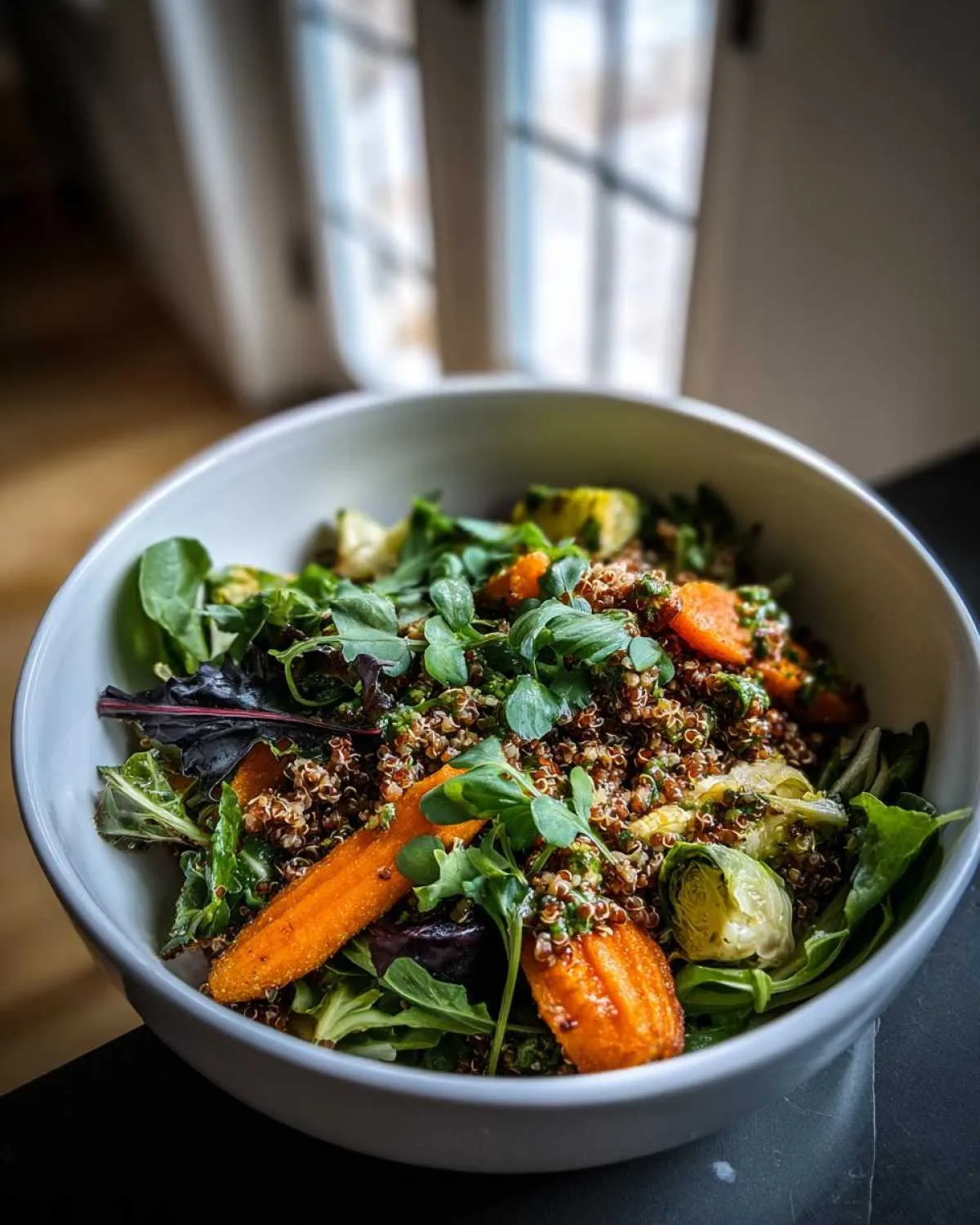 A close-up of a plant powered greens salad bowl filled with quinoa, roasted carrots, Brussels sprouts, and fresh greens.