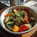 A vibrant plant powered greens salad bowl filled with quinoa, roasted zucchini, bell peppers, and mushrooms, topped with fresh herbs.