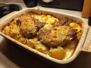 A close-up of a creamy pork chop and potato casserole baked in a dish, topped with melted golden cheese.