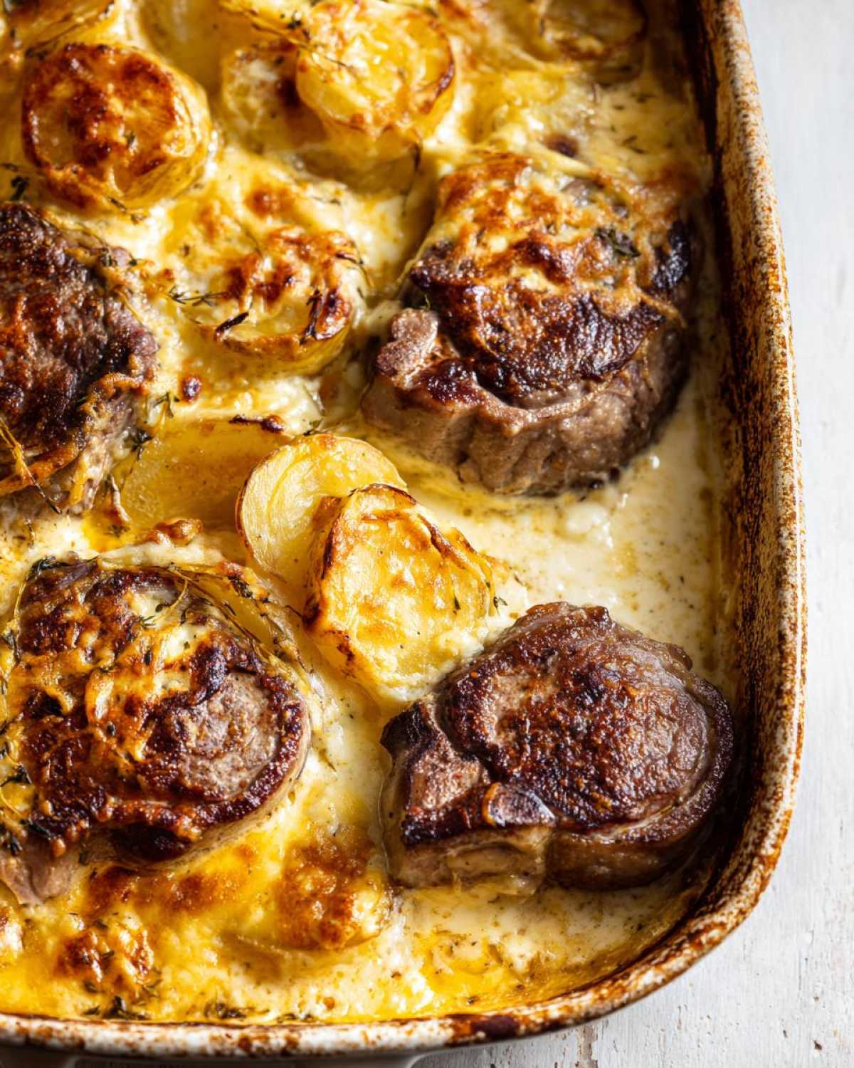 Close-up of a creamy pork chop and potato casserole in a baking dish, featuring browned pork chops and golden-brown potato slices.