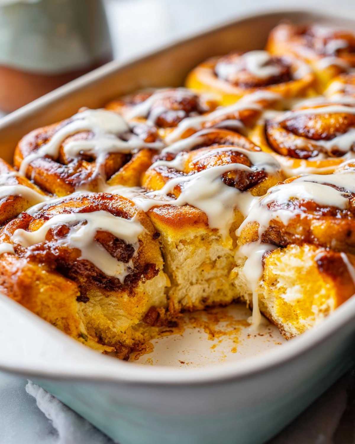Close-up of a gooey pumpkin cinnamon roll bake drizzled with white icing in a baking dish.