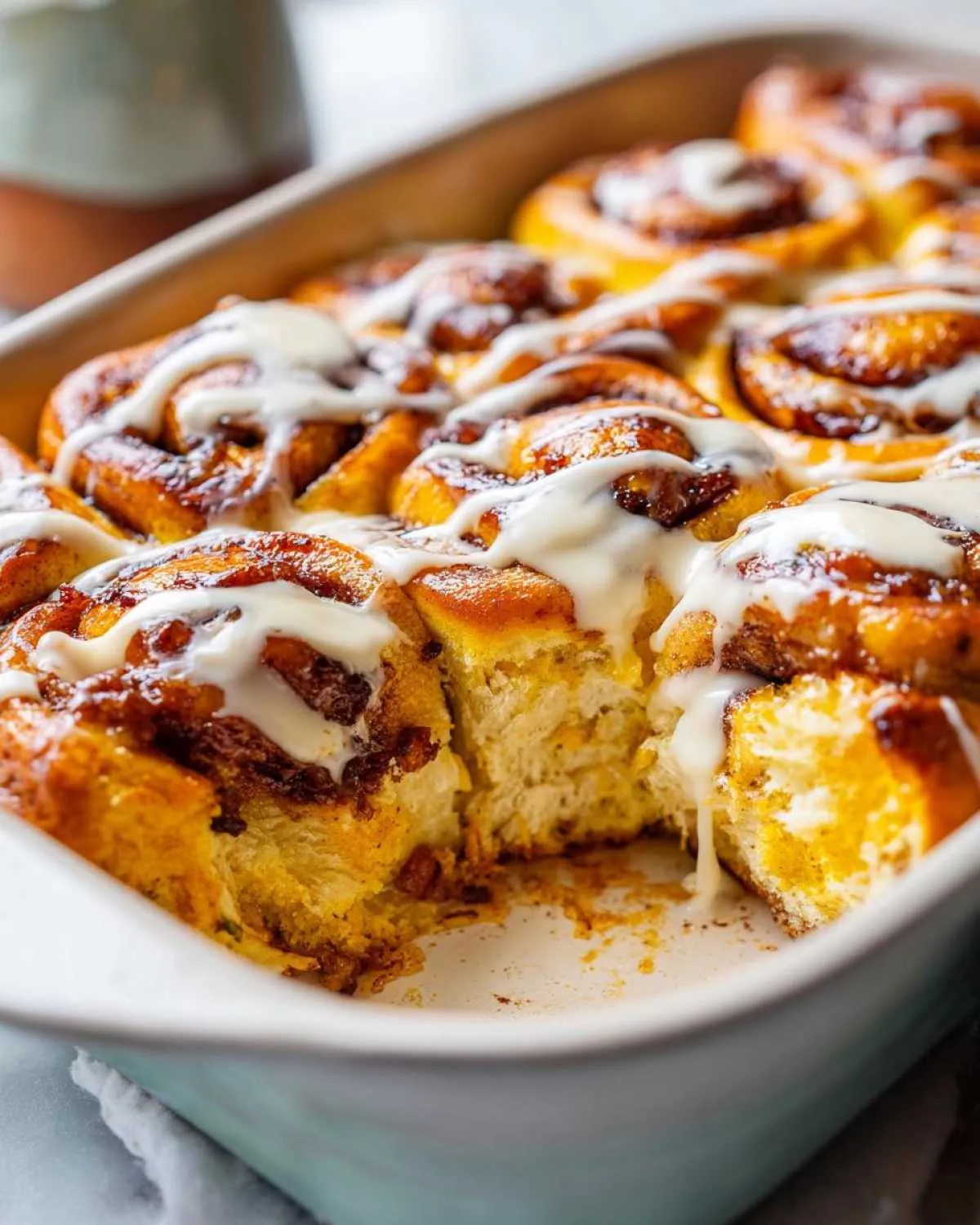 Close-up of a gooey pumpkin cinnamon roll bake drizzled with white icing in a baking dish.