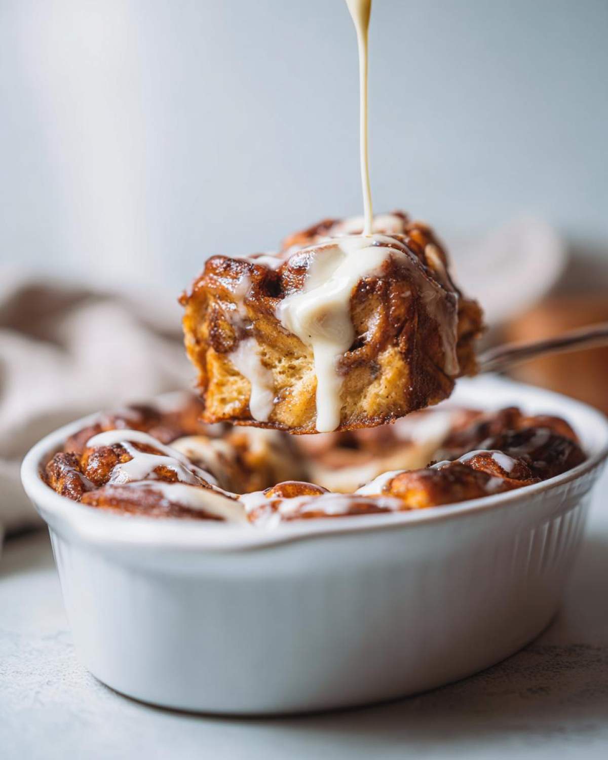 A fork lifts a piece of gooey pumpkin cinnamon roll bake, drizzled with white glaze.