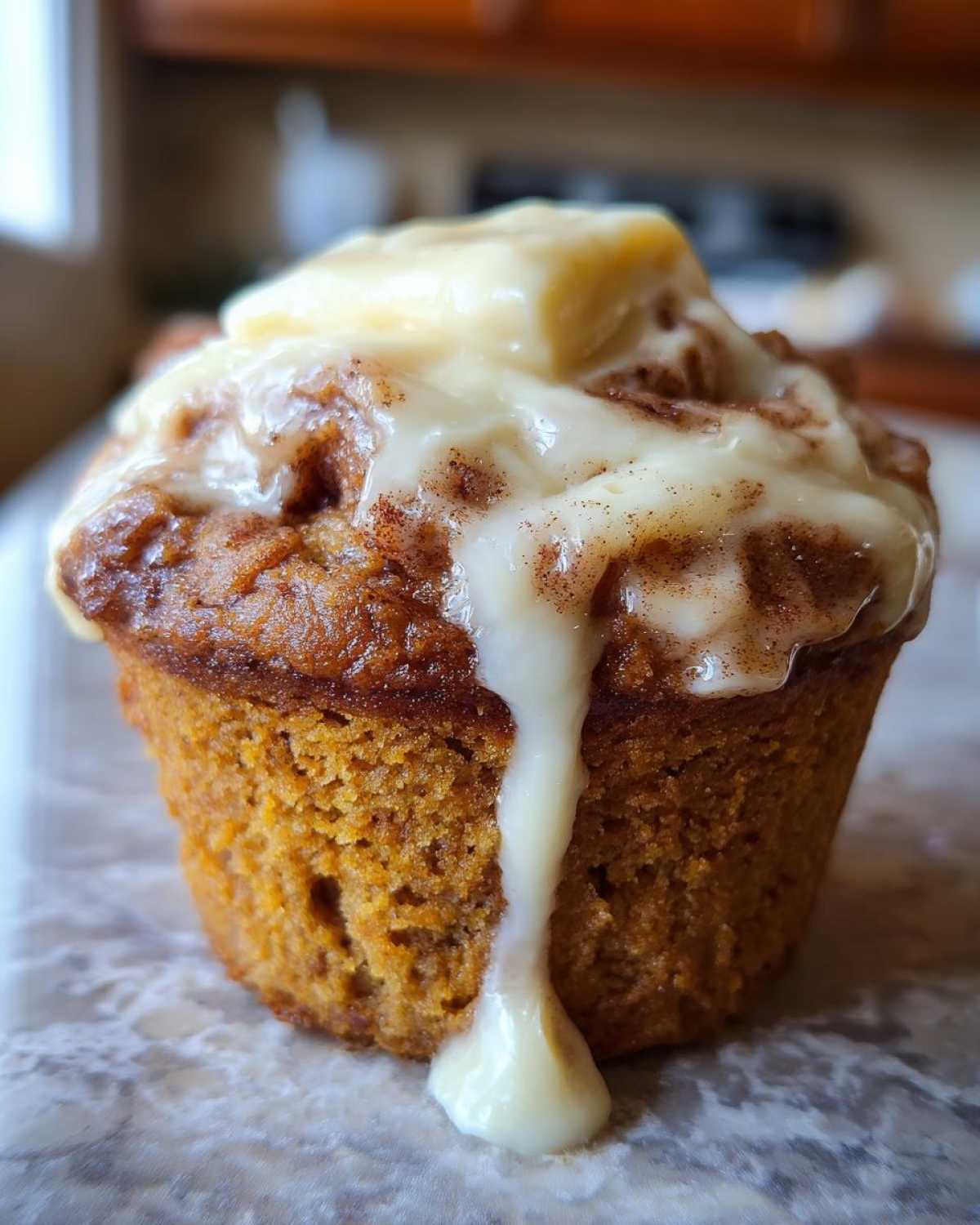 Close-up of a moist pumpkin cinnamon roll muffin topped with a generous swirl of cream cheese glaze.
