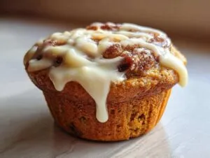 Close-up of a moist pumpkin cinnamon roll muffin topped with creamy white glaze.