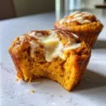Close-up of a delicious pumpkin cinnamon roll muffin with a bite taken out, topped with glaze.