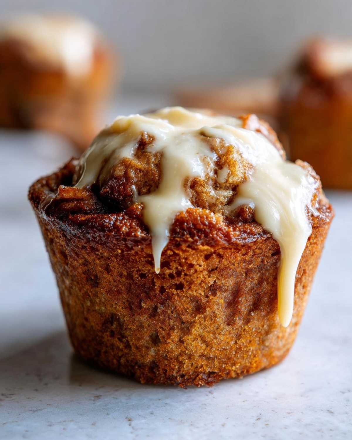 Close-up of a moist pumpkin cinnamon roll muffin topped with creamy white glaze.