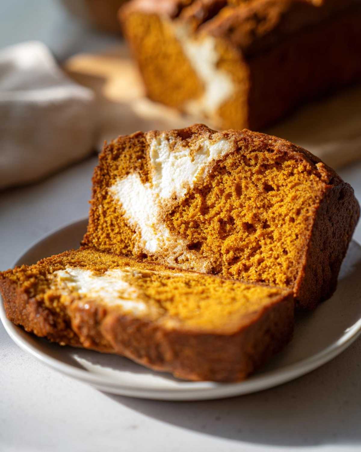 Close-up of a slice of moist pumpkin cream cheese bread with a creamy swirl.