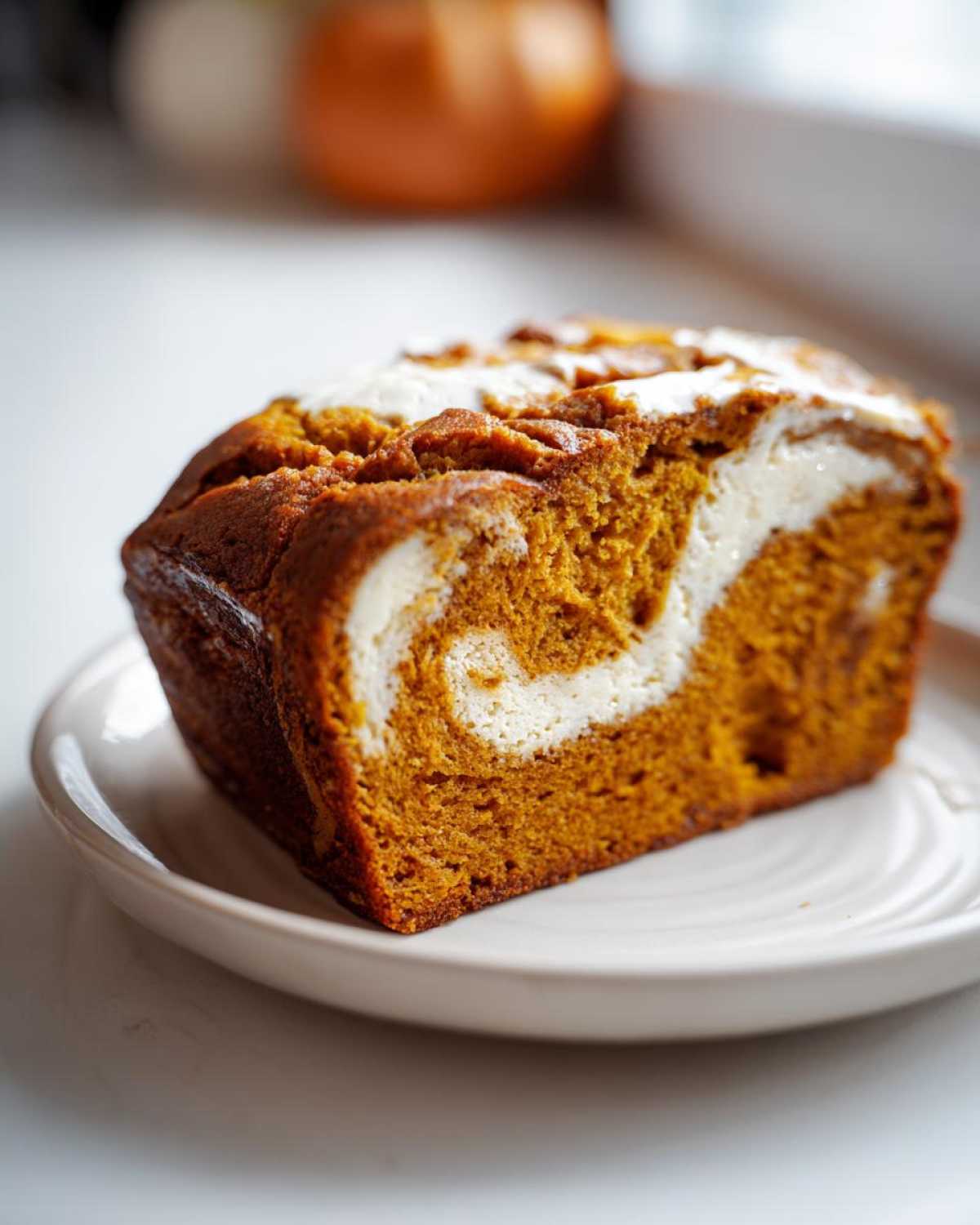 A slice of moist pumpkin cream cheese bread with visible cream cheese swirls on a white plate.