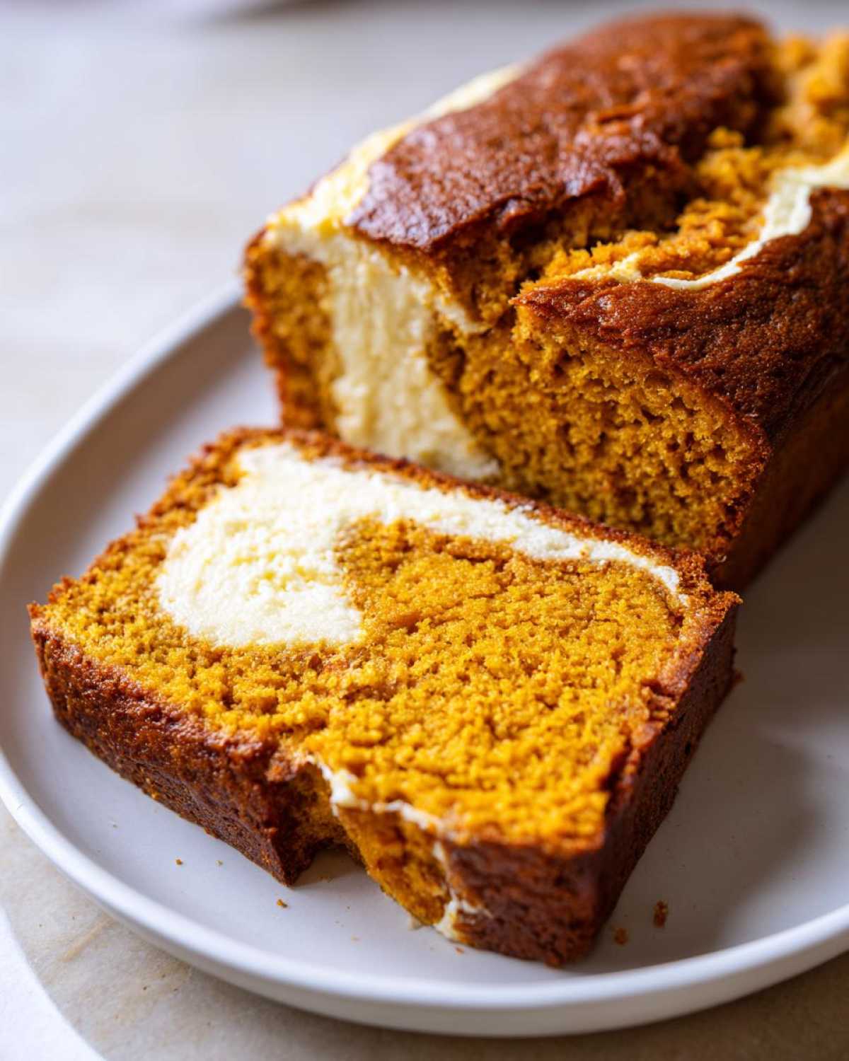 Close-up of a slice of moist pumpkin cream cheese bread with a prominent cream cheese swirl.
