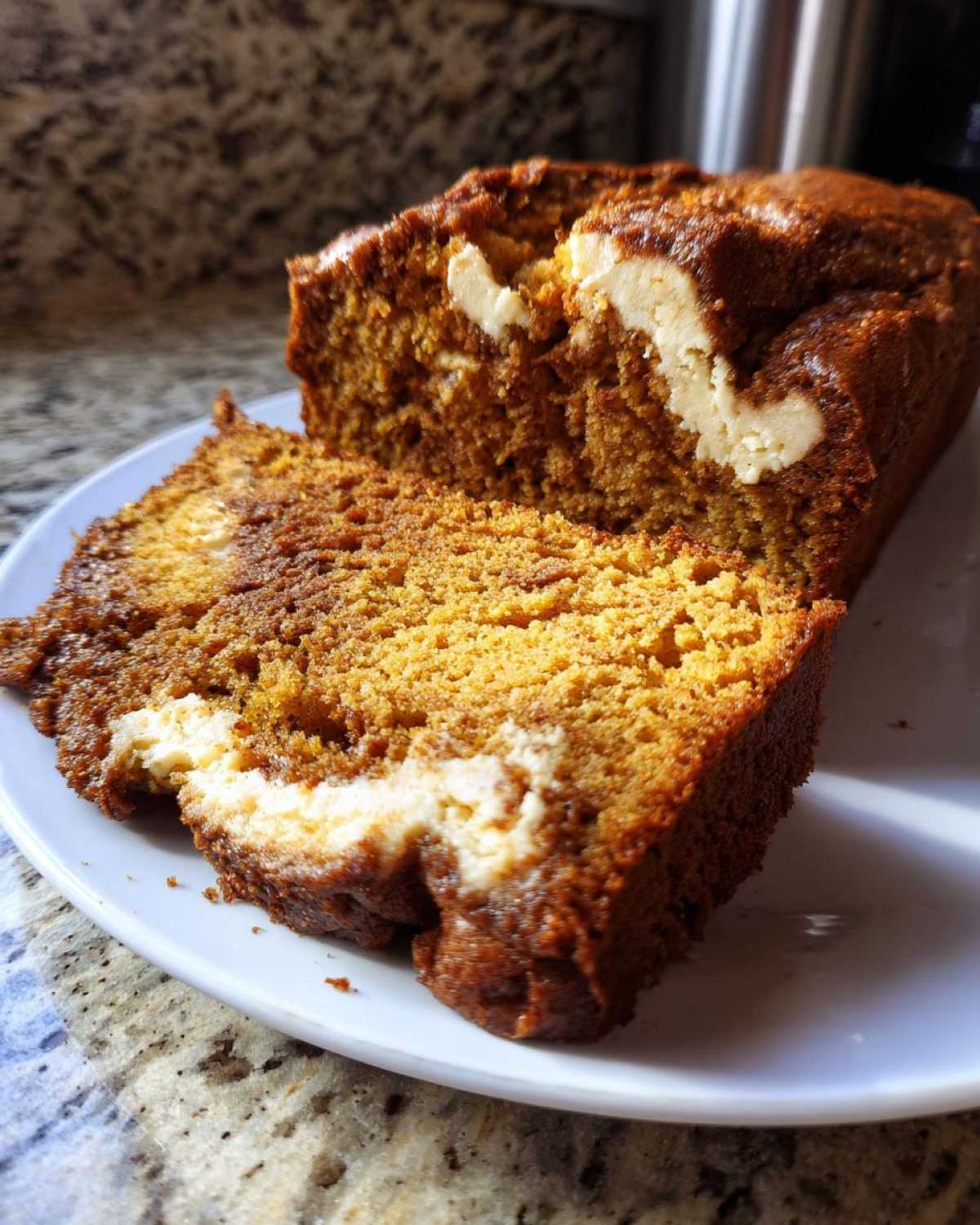 A close-up of a slice of moist pumpkin cream cheese bread with visible swirls of cream cheese.