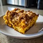A close-up of a moist slice of pumpkin dump cake with a crumb topping on a white plate.