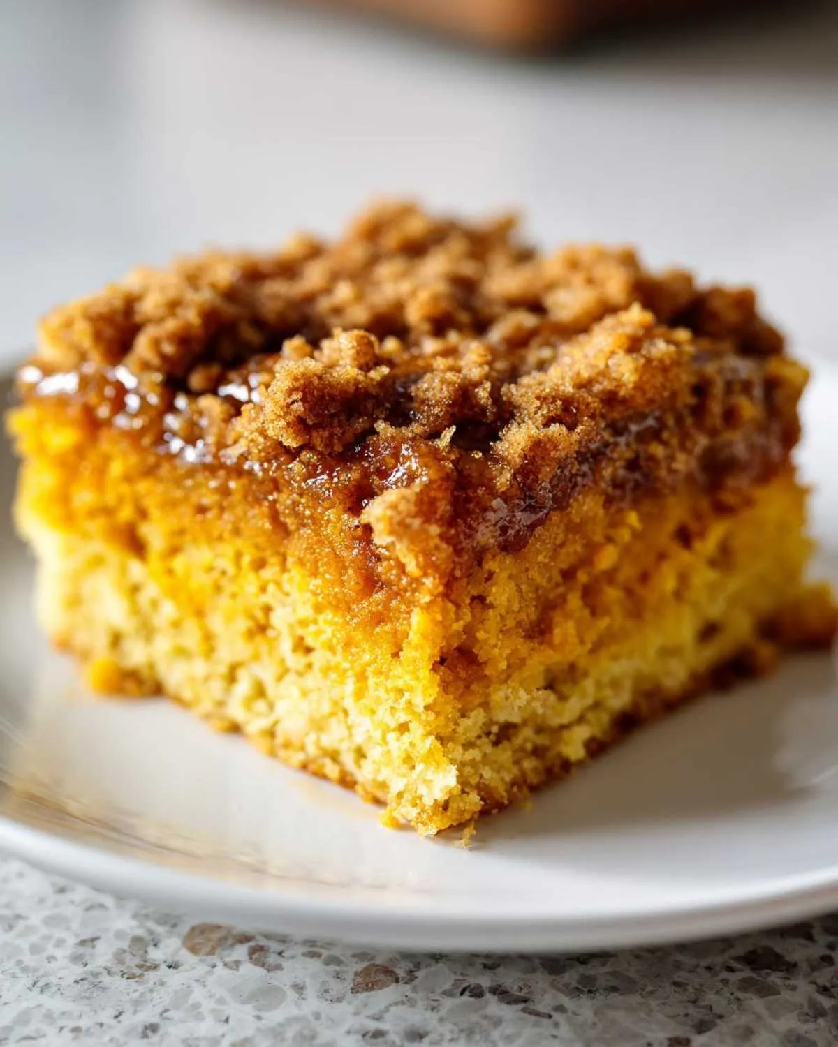 A close-up shot of a moist slice of pumpkin dump cake on a white plate, topped with crumbly brown sugar topping.