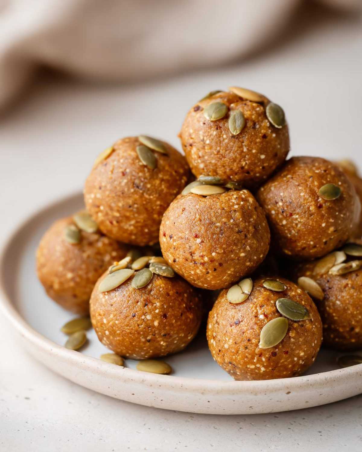 A stack of delicious pumpkin protein bites topped with pumpkin seeds on a light-colored plate.