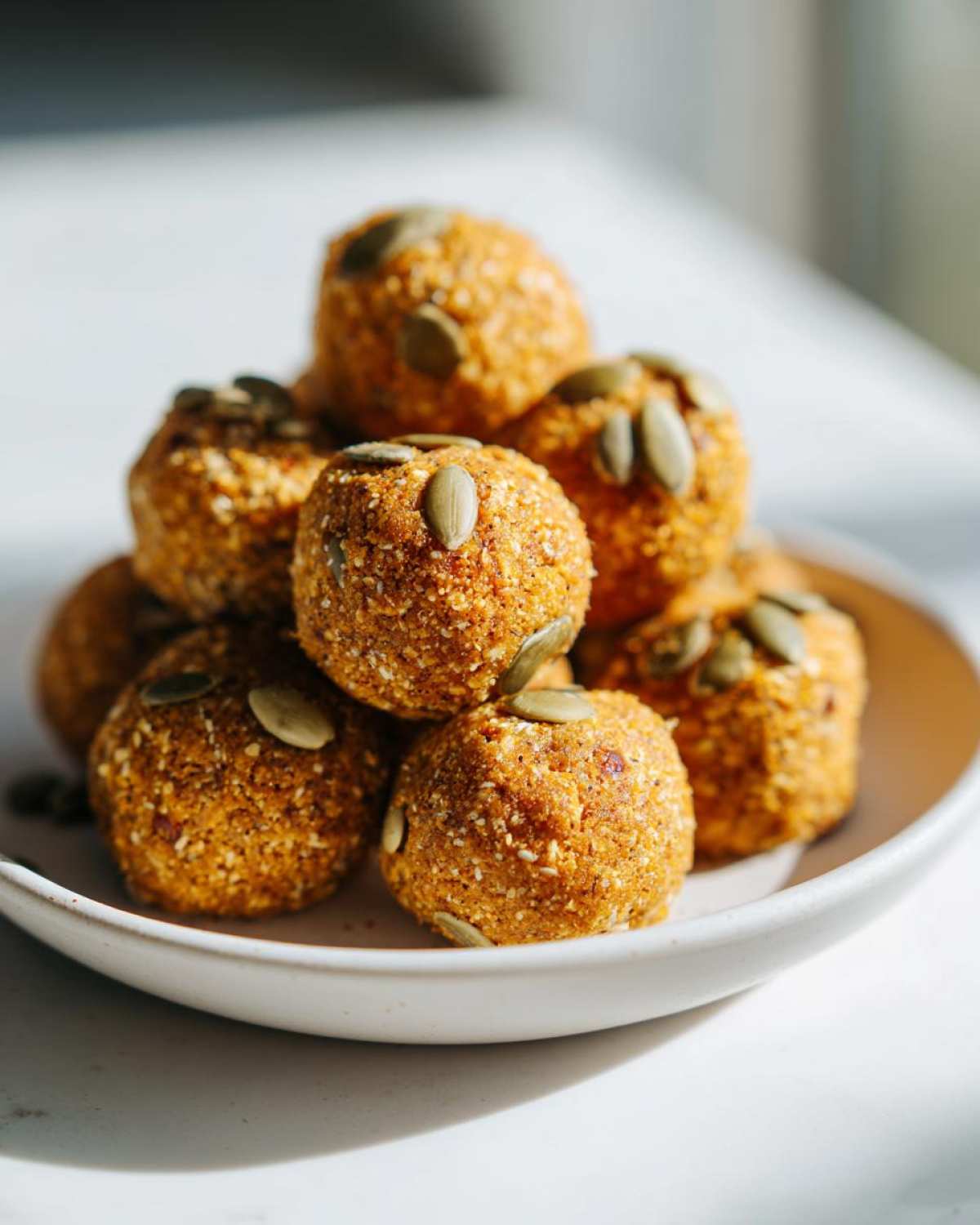 A stack of delicious pumpkin protein bites topped with pumpkin seeds on a white plate.