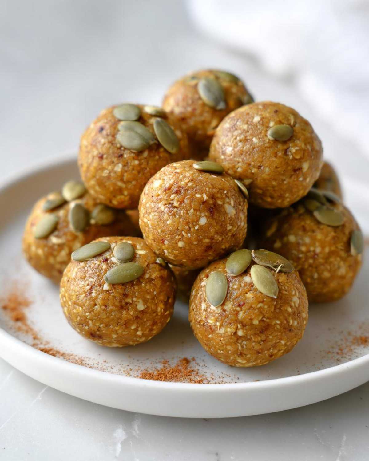 A close-up of a pile of pumpkin protein bites topped with pumpkin seeds on a white plate.
